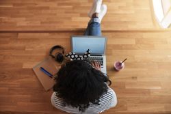 Overhead shot of woman sitting on wooden floor and working on laptop with healthy smoothie