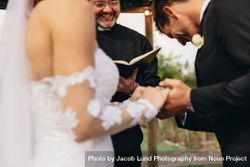 Couple holding hands with groom acknowledging the consent before the priest 5aGE8b