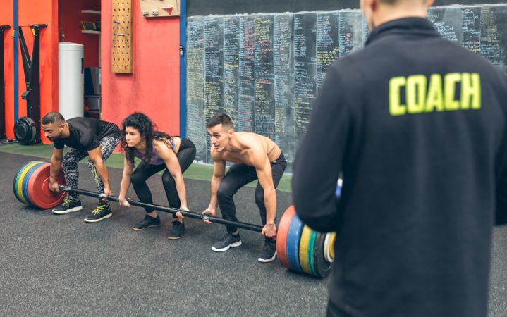 Multiracial team lifting weights in the gym with their coach