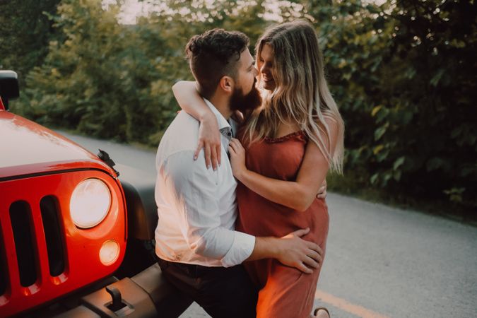 Loving couple sitting on car on road near forest