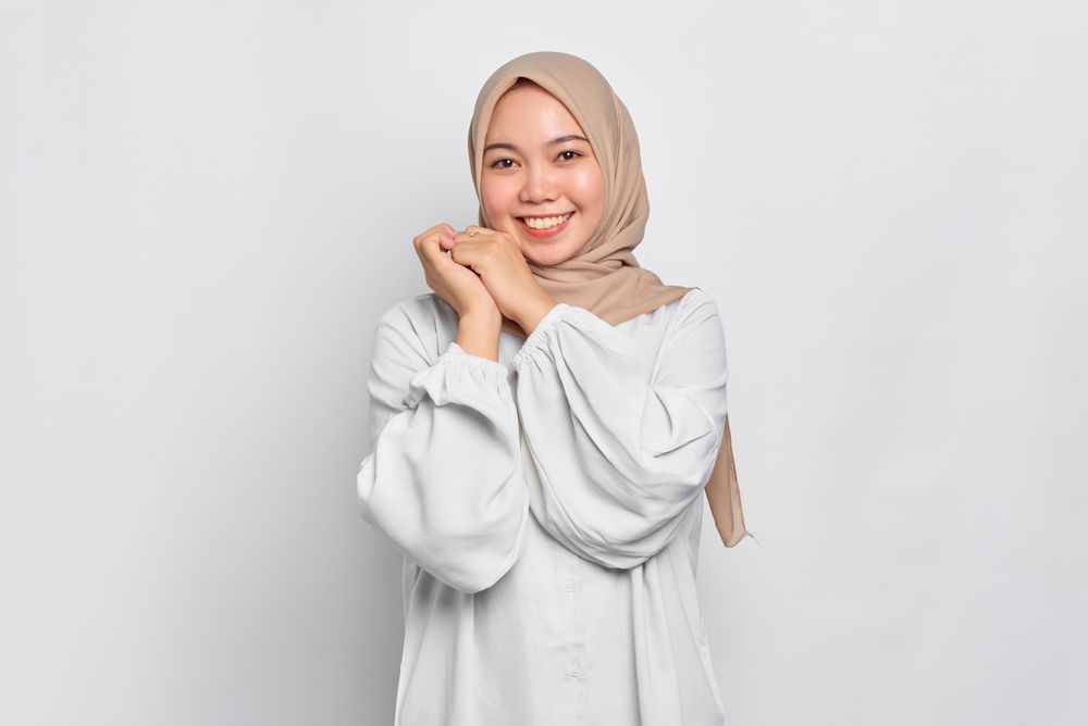 Smiling Asian female in headscarf with hands up to side of cheek