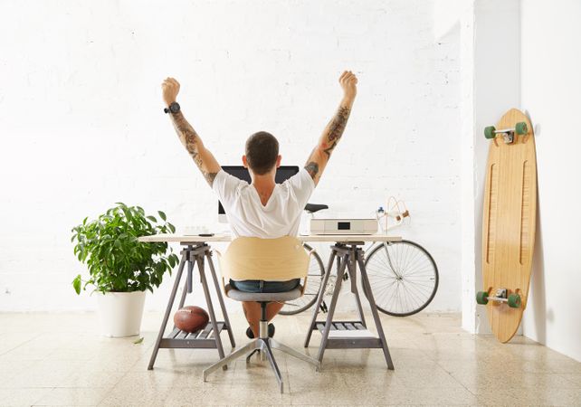 Back view of man stretching at his home office desk