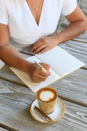 Crop woman writing in notepad while sitting in outdoor cafe with