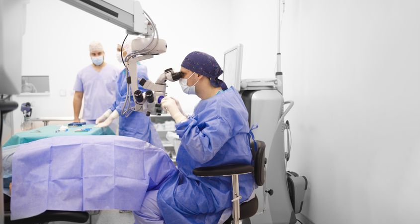 Doctor looking through eye equipment while performing a cataract surgery