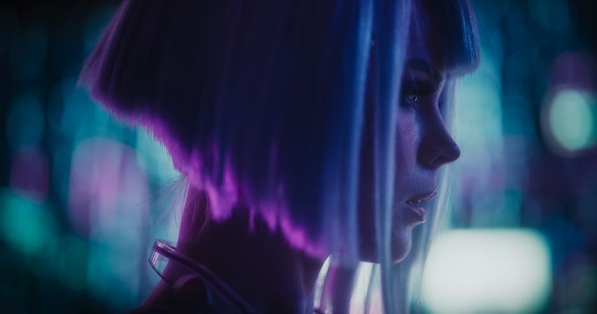 Close Up Portrait of a Stylish Young Cosplay Model with Blue Hair Looking at a Futuristic Cybernetic City with Neon Lights. Young Excited Female in a Cyberpunk Augmented Reality