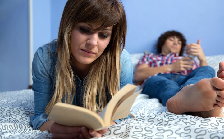 Woman reading a book lying in bed with boyfriend