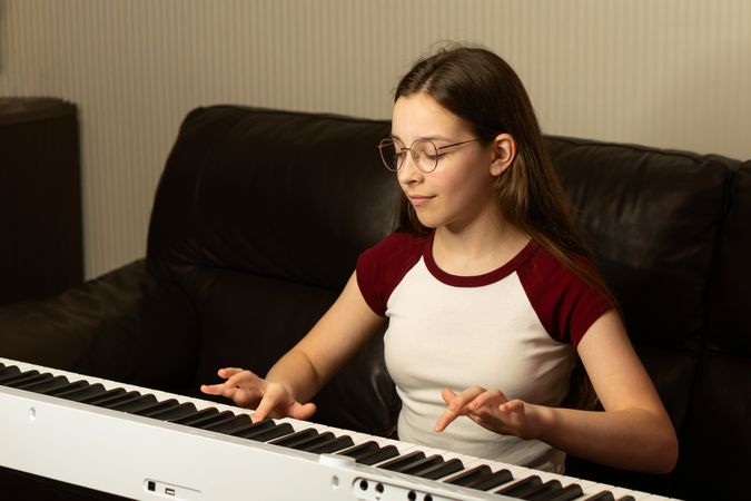 Young girl in glasses playing the piano, focused and relaxed.