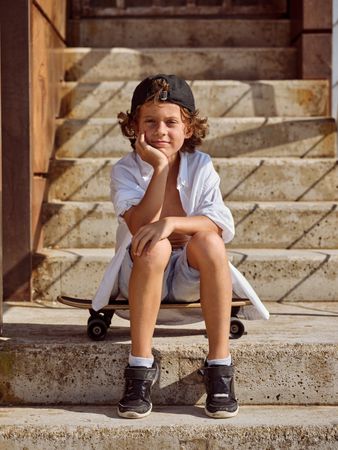 Smiling boy sitting on skateboard looking at camera