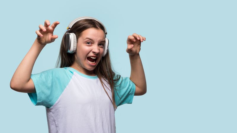 Girl making scary face with hands raised while wearing headphones.