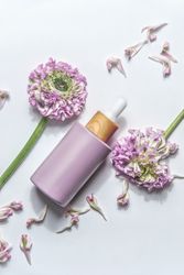 Pastel purple cosmetic bottle with pipette and beautiful flowers and petals