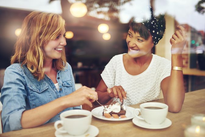 Two female friends sitting at a cafe table chatting and laughing with coffee and pastry