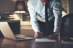 Professional man in shirt and tie signing documents at his desk