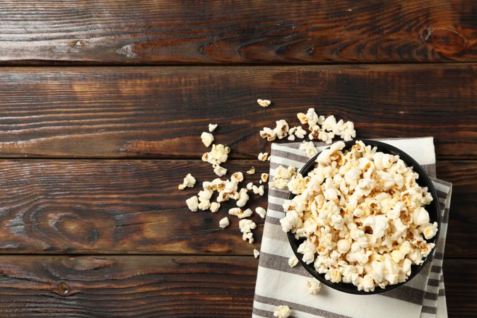 Towel and bowl with popcorn on wooden background, copy space