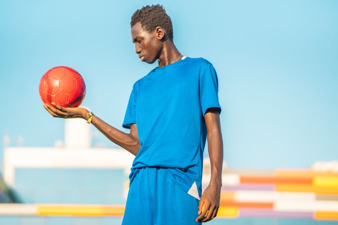Black teenager with football ball against sky