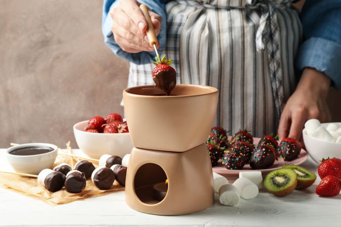 Woman dipping strawberry in chocolate. Delicious chocolate fondue