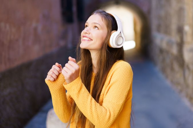 A Joyful Young Woman Enthusiastically Listening to Music While Strolling in a Scenic Alley