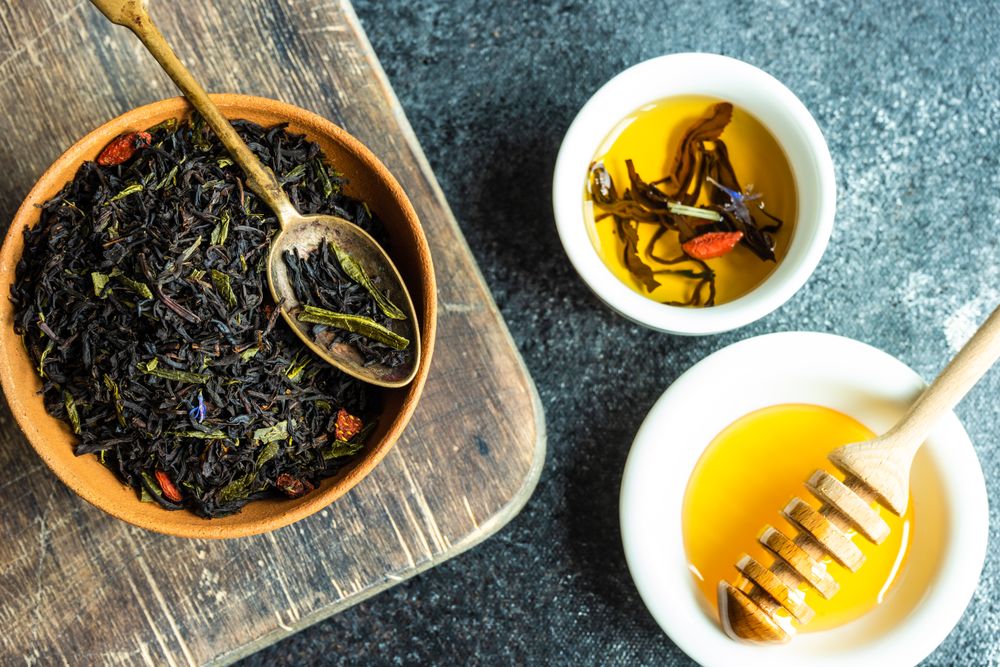 Fragrant loose leaf tea in bowl on counter with honey and dipper
