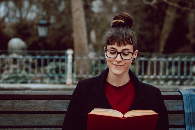 Young woman reading book on bench in park
