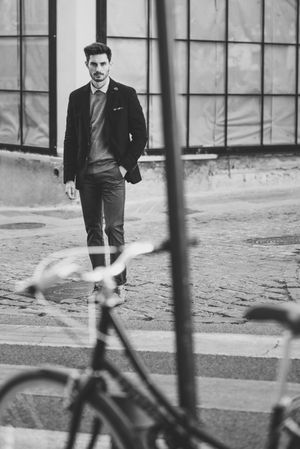 Moody shot of man in the street wearing elegant suit with vintage bicycle in foreground, b&w