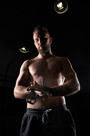 Muscular sportsman preparing hands with chalk for exercise