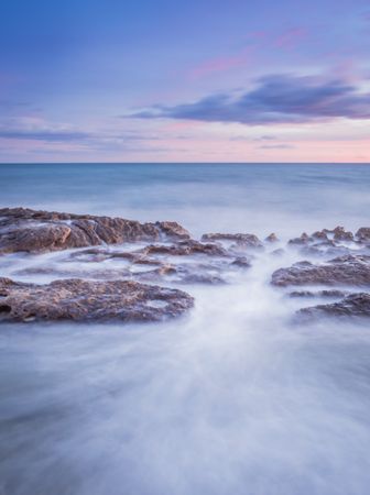 Sea waving near rough rocks during sunset
