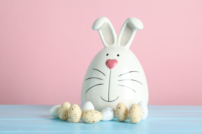 Decorated bunny and Easter eggs on table against color background. Space for text
