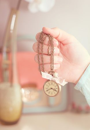 hand holding a vintage clock necklace in front of female complements in soft pastel colors