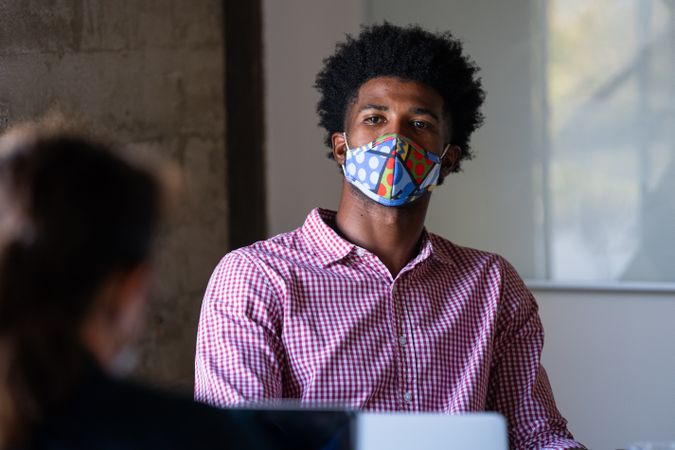 Man in brightly colored face mask talking with a a co-working at the office