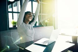 Woman sitting with laptop in cafe and stretching