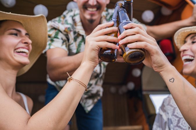 Smiling friends clinking bottles of beer celebrating vacation
