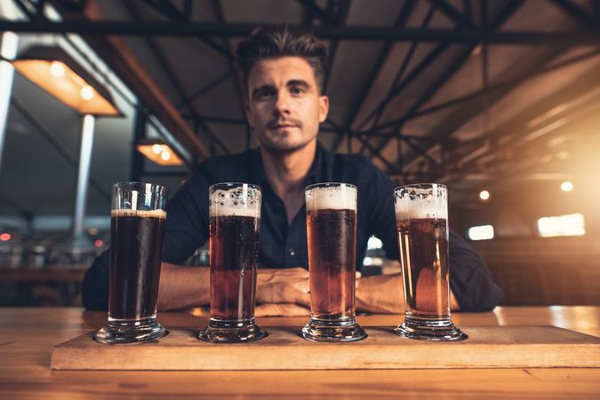 Young man tasting different varieties of craft beer on wooden table at brewery