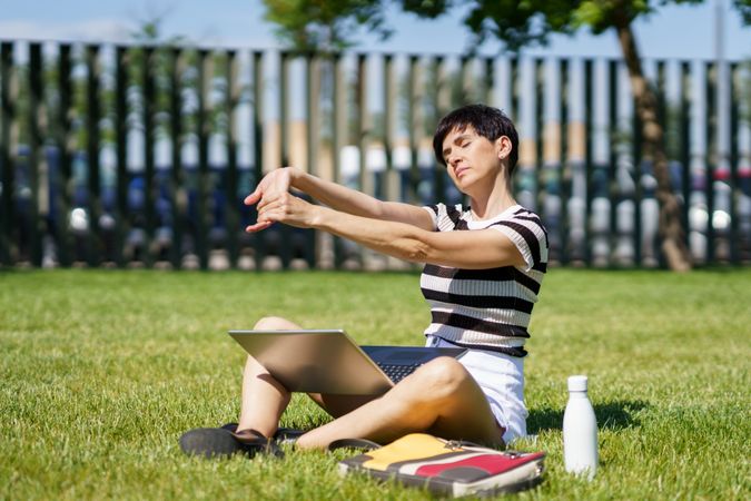 Woman stretching in grassy park with computer on lap