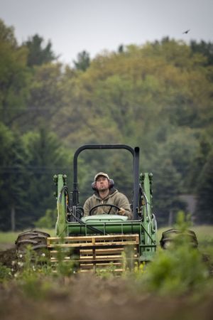 Copake, New York - May 19, 2022: Man on tractor in muddy field, vertical