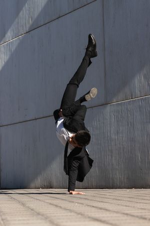Asian businessman performing breakdance handstand on street
