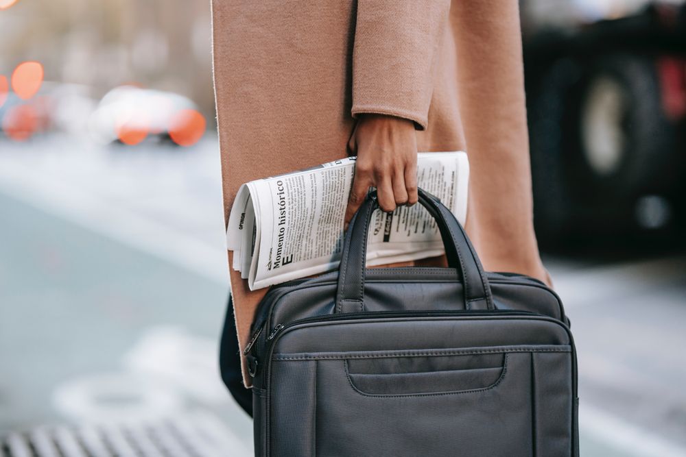 Person in pink coat holding a newspaper and suitcase