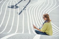 Modern relaxed woman on marked road and browsing smartphone