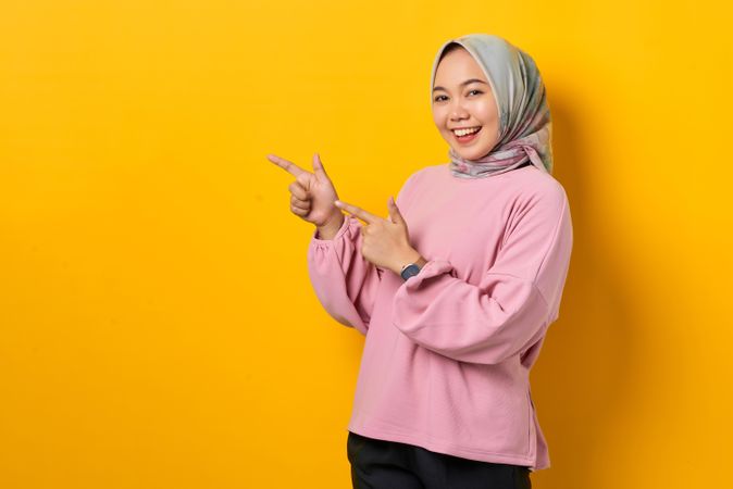 Happy Muslim woman in headscarf pointing to space beside her