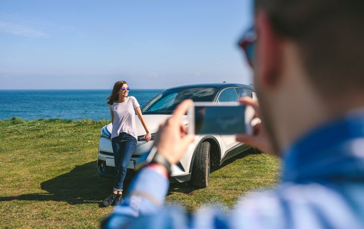 Guy taking picture of girlriend leaning on a car