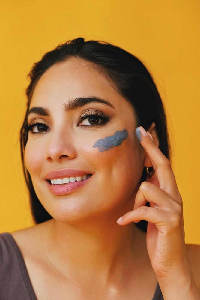 Happy Latina woman applying clay mask with hand