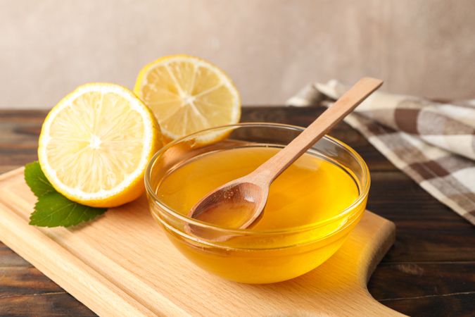 Lemons and bowl with honey and dipper on wooden background, space for text