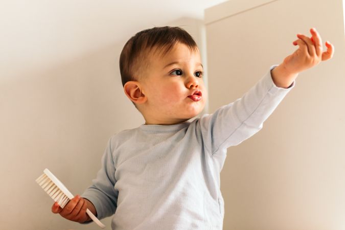 adorable baby sitting with a hair brush pointing at something