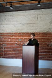 Nonbinary person standing at podium with microphone bElJV4