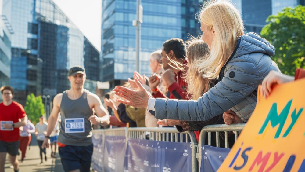 Portrait of a Male Marathon Runner Giving a High Five to Female Family Member in the Audience While Running.
