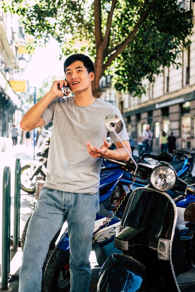 Confident Asian man talking on phone while standing by motorbike