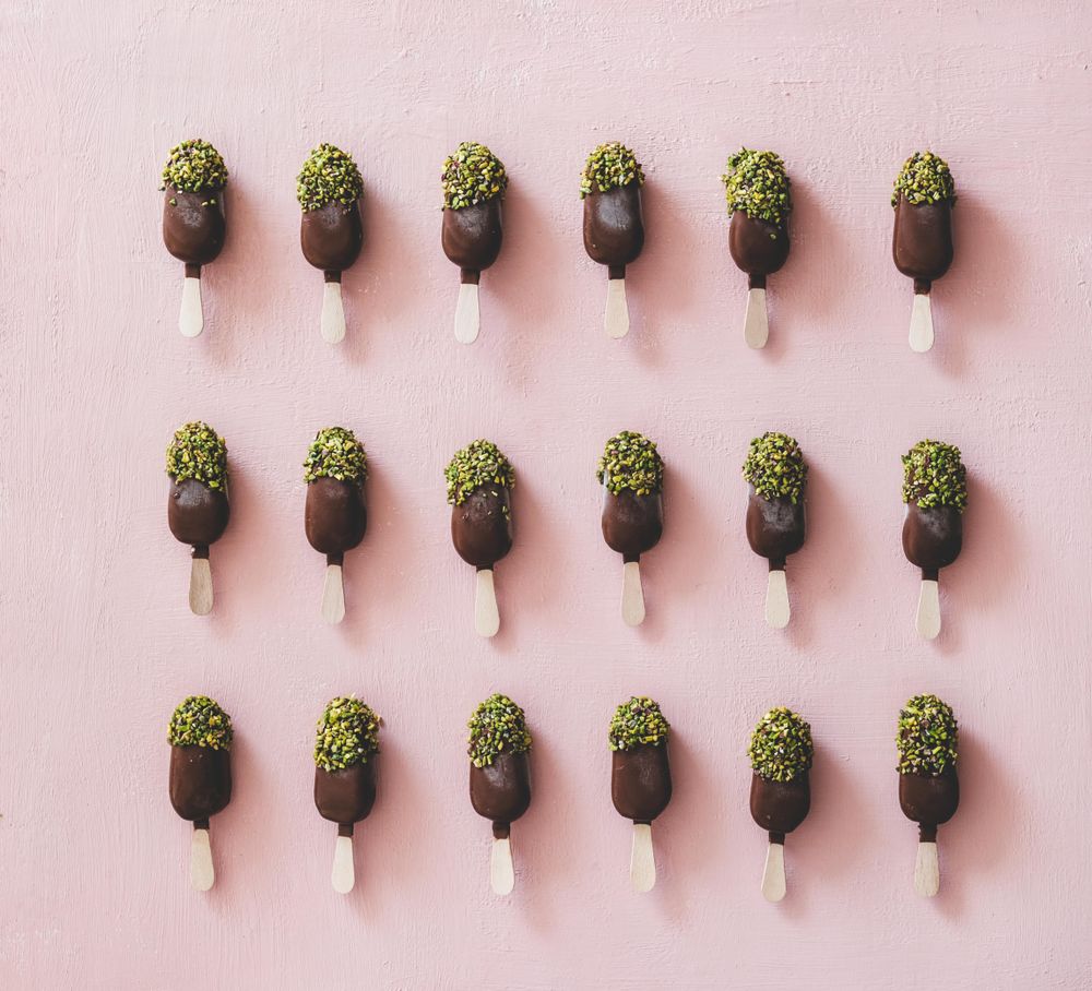 Rows of ice cream chocolate pistachio popsicles, pink background