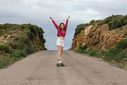 Smiling woman raising hands while riding longboard
