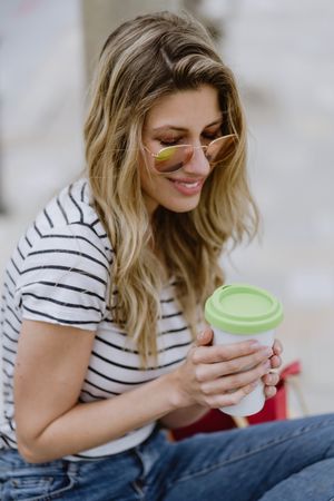 Happy woman with disposable cup of coffee sitting on street bench
