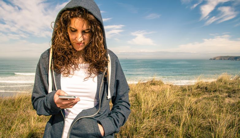 Woman checking phone with ocean in background