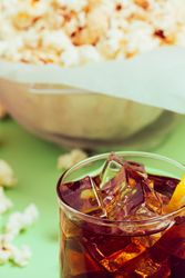 Popcorn in bowl near drink in glass with ice and lemon