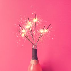 Champagne bottle with sparklers on pink background
